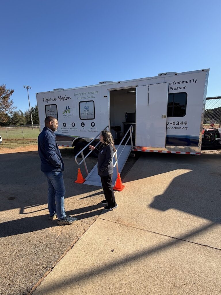 Two people standing beside Hands of Hope Clinic’s Hope in Motion mobile healthcare unit at Heritage Park in McDonough.